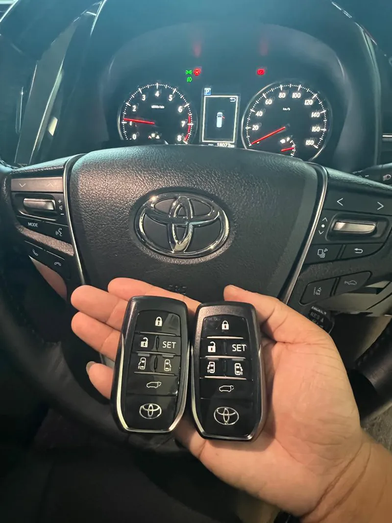 Two duplicated Toyota smart key fobs held in front of a Toyota steering wheel