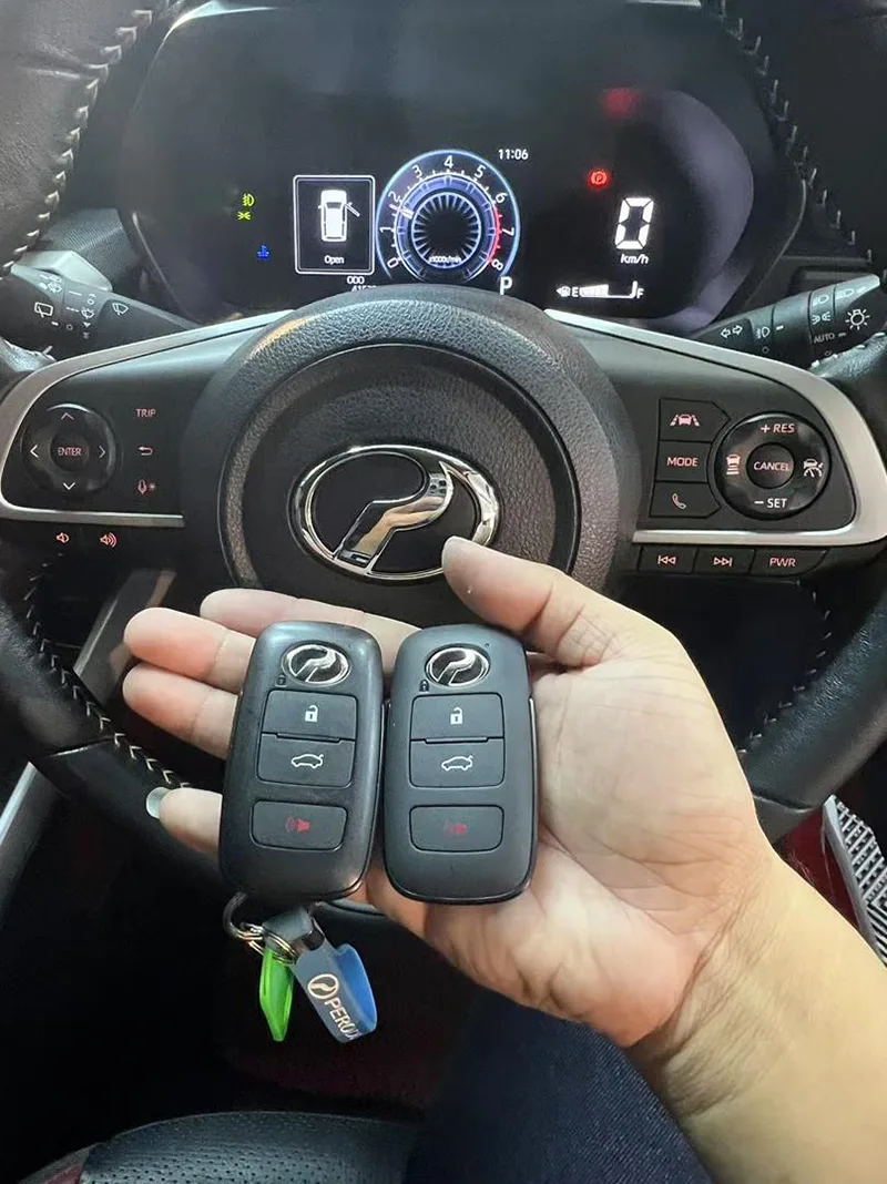 Two Perodua smart key fobs copied, held at a Perodua steering wheel