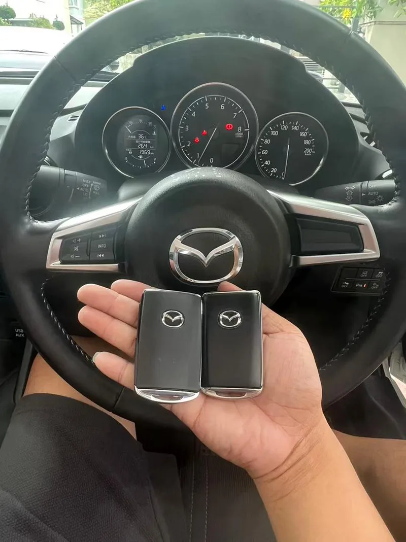 Two Mazda smart keys duplicated, held at a Mazda steering wheel