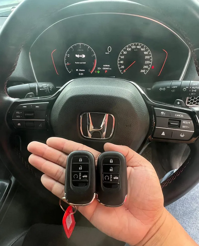 Two Honda smart key fobs programmed, held at a Honda steering wheel